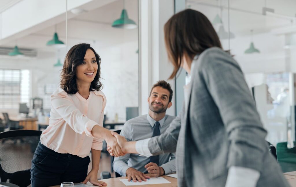 Office Management Zwei Frauen in Geschäftskledung reichen sich die Hände.